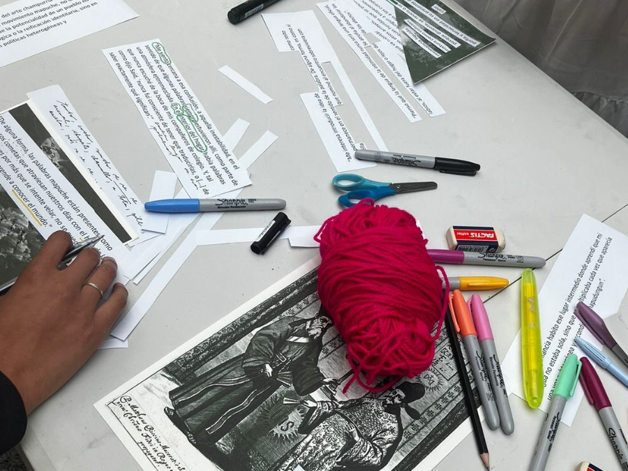 Mesa de trabajo con materiales de escritura, impresos y lana fucsia utilizados en una actividad creativa del taller “Sutura de las aguas”.